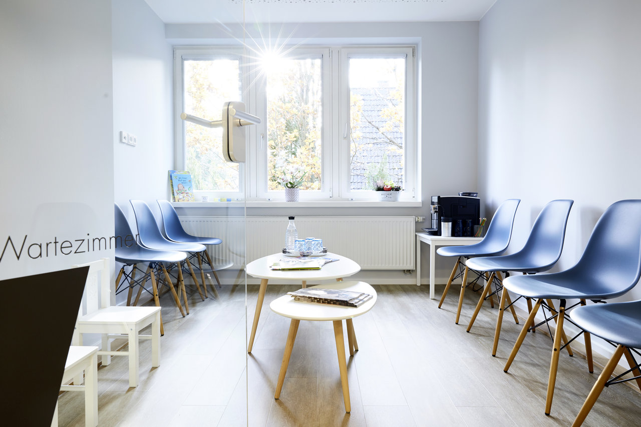 Das Wartezimmer. Blick von der Zimmertür auf Wartestühle für Kinder und Erwachsene. Zeitschriften und Getränke auf dem Tisch.